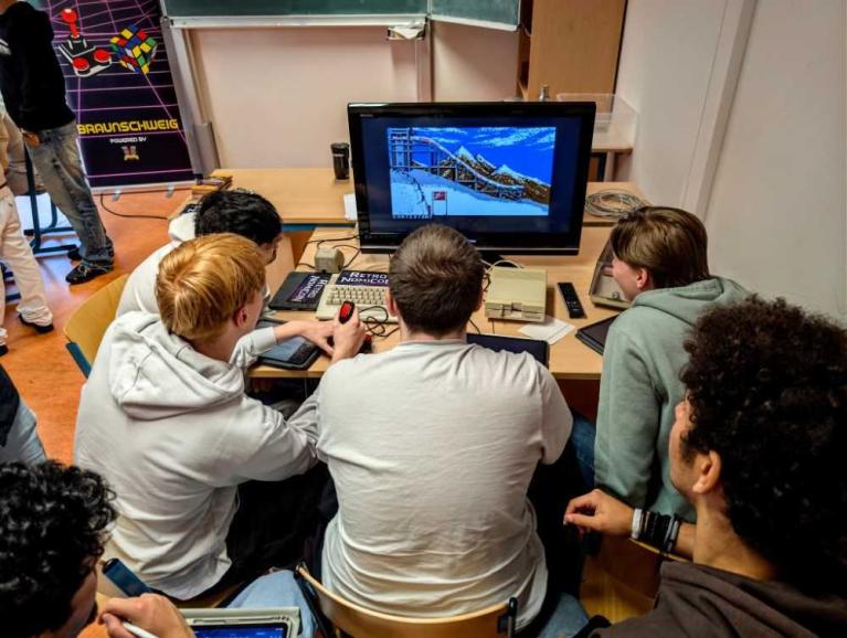 Mehrere Jugendliche sitzen an einem Tisch vor einem Monitor und nutzen einen Retro-Computer.