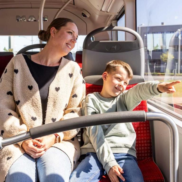 Eine Frau und ein Junge sitzen zusammen im Bus, der Junge zeigt nach draußen.