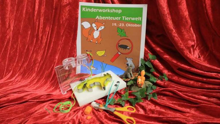 Bastelmaterialien vor einem Plakat für einen Kinderworkshop zum Thema Tierwelt