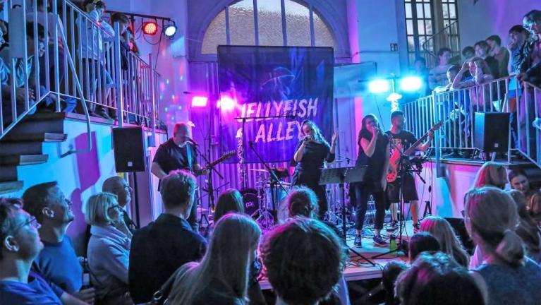 Liveband spielt auf kleiner Bühne vor Publikum in einem beleuchteten Innenraum