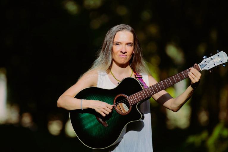 Eine Frau spielt im Freien Gitarre und blickt in die Kamera.