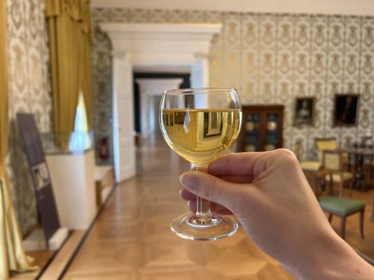 Eine Hand hält ein Glas mit weißem Wein in einem eleganten Raum