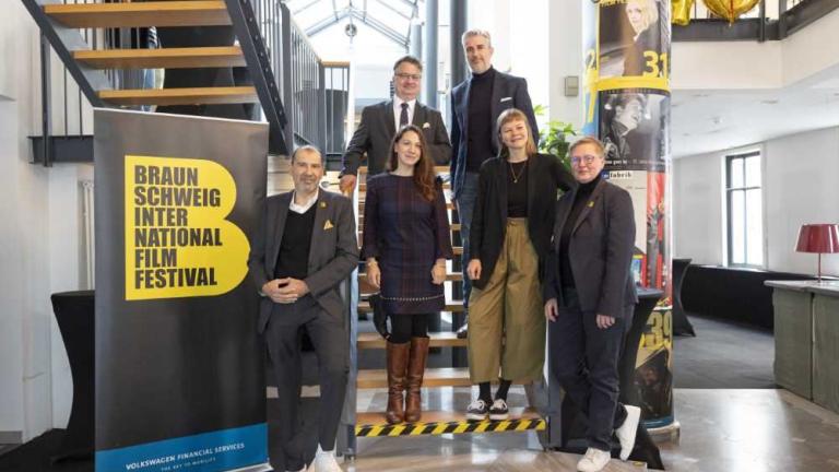 Sechs Personen posieren auf einer Treppe neben einem Banner des Braunschweig International Film Festival.