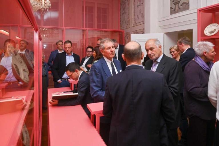 Mehrere Männer und Frauen in Anzügen stehen in einem Raum mit roten Vitrinen und betrachten Ausstellungsstücke