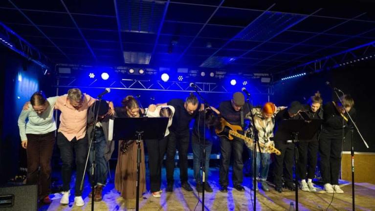 Eine Gruppe von Musikerinnen und Musikern verbeugt sich auf einer Bühne mit blauer Beleuchtung.