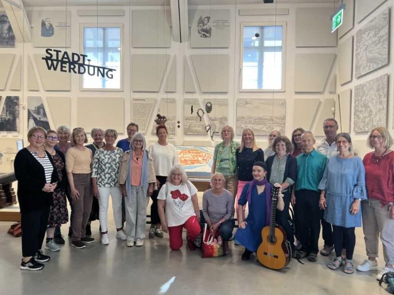 Gruppe von Menschen in einem Ausstellungsraum mit historischen Bildern und einer Gitarre