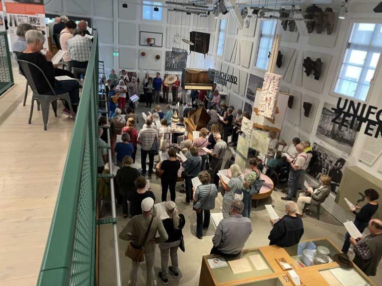 Menschenmenge in einem Museum oder Ausstellungsraum, viele lesen Blätter und stehen um Exponate herum