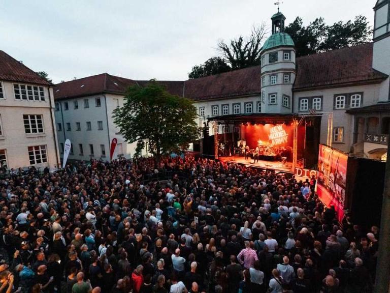 Große Menschenmenge vor einer Bühne bei einem Open-Air-Konzert in einem Innenhof