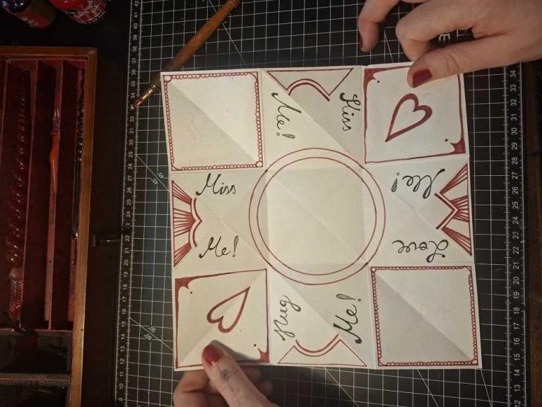 Eine Hand hält eine dekorierte, quadratische Faltkarte mit Herzmotiven und den Worten Kiss Me und Miss Me.