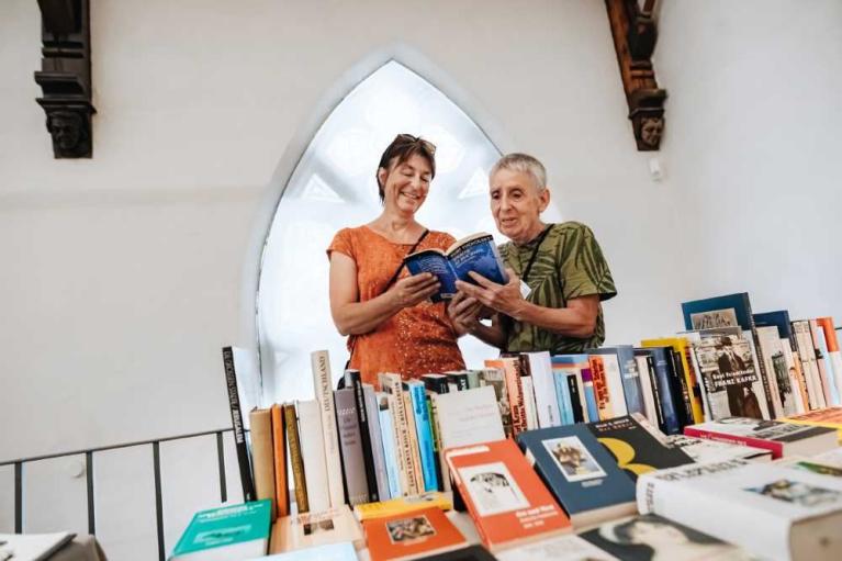 Zwei Frauen betrachten gemeinsam ein Buch an einem Büchertisch mit vielen Büchern