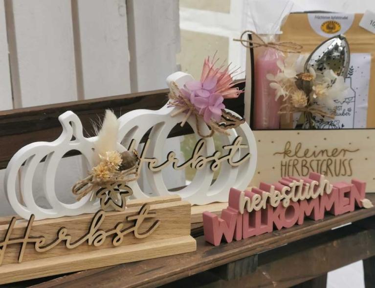Dekorative Herbstschilder mit Kürbisform, Trockenblumen und Schriftzügen auf einer Holzfläche