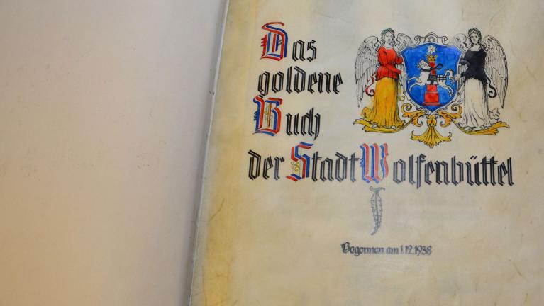 Aufgeschlagene Buchseite mit dem Titel Das goldene Buch der Stadt Wolfenbüttel und Wappen