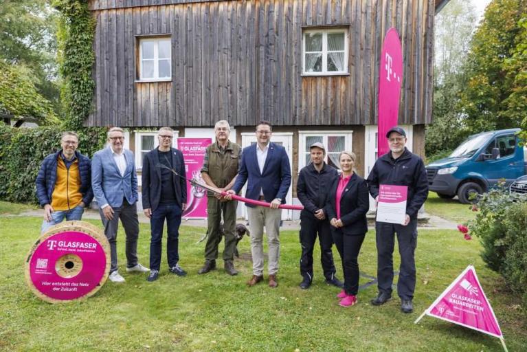 Gruppe von sieben Personen bei einem Glasfaser-Pressetermin vor einem Holzhaus