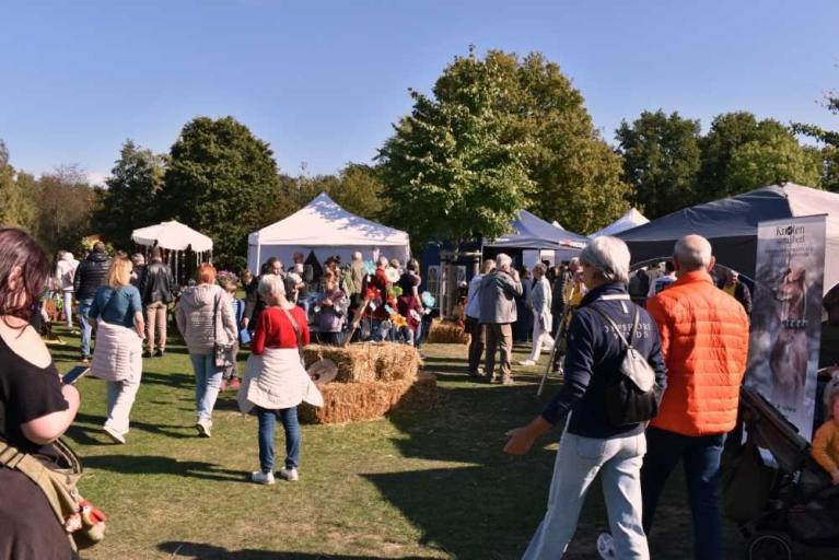 Menschen schlendern über ein herbstliches Freiluftfest mit Zelten und Heuballen auf einer Wiese