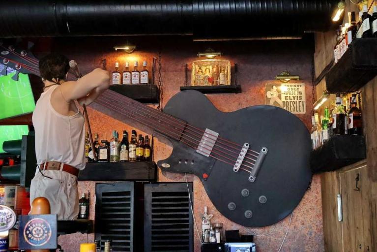 Ein Mann steht in einer Bar neben einer riesigen Gitarrenwanddekoration mit Flaschenregalen