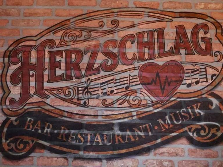 Schriftzug Herzschlag auf einer Ziegelwand mit Musiknoten und Herzsymbol