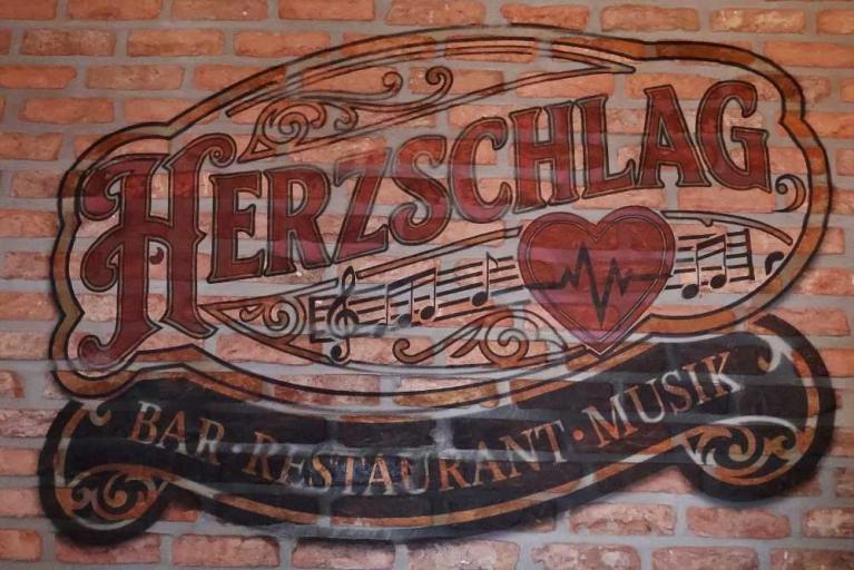 Schriftzug Herzschlag auf einer Ziegelwand mit Musiknoten und Herzsymbol
