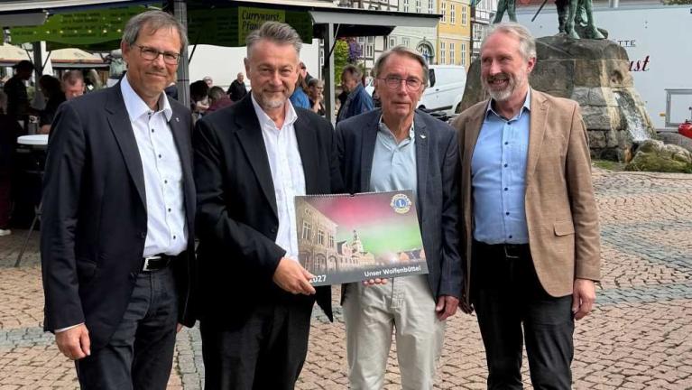 Vier Männer stehen im Freien und halten gemeinsam einen Kalender mit der Aufschrift Unser Wolfenbüttel