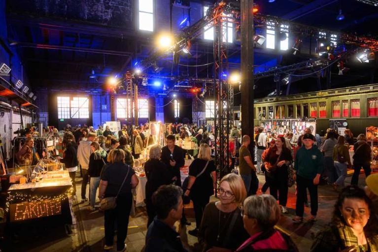 Menschenmenge auf einem beleuchteten Indoor-Markt mit Verkaufsständen in einer großen Halle