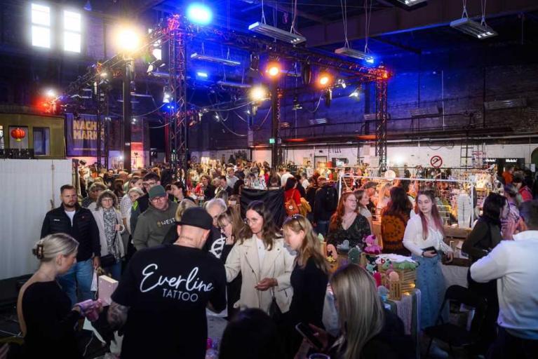 Menschenmenge auf einer Messe in einer großen Halle mit Ständen und Beleuchtung
