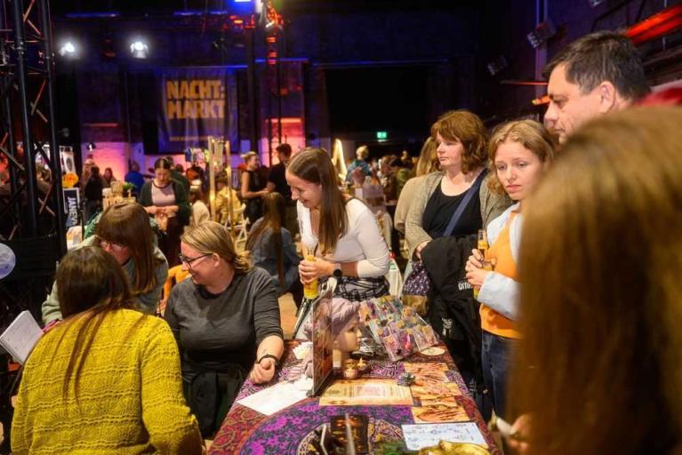 Menschen auf einem belebten Markt an einem Verkaufsstand in einer Halle