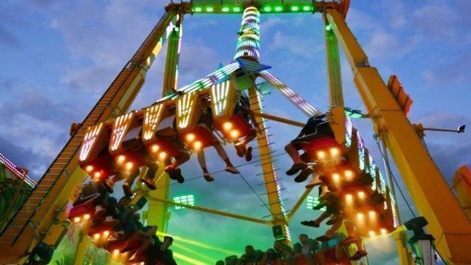 Beleuchtetes Fahrgeschäft auf einem Volksfest mit schwebenden Sitzreihen bei Dämmerung