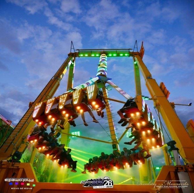 Beleuchtetes Fahrgeschäft auf einem Volksfest mit schwebenden Sitzreihen bei Dämmerung