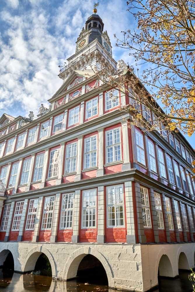 Historisches Gebäude mit roter Fassade, vielen Fenstern und Turm über einem Wassergraben
