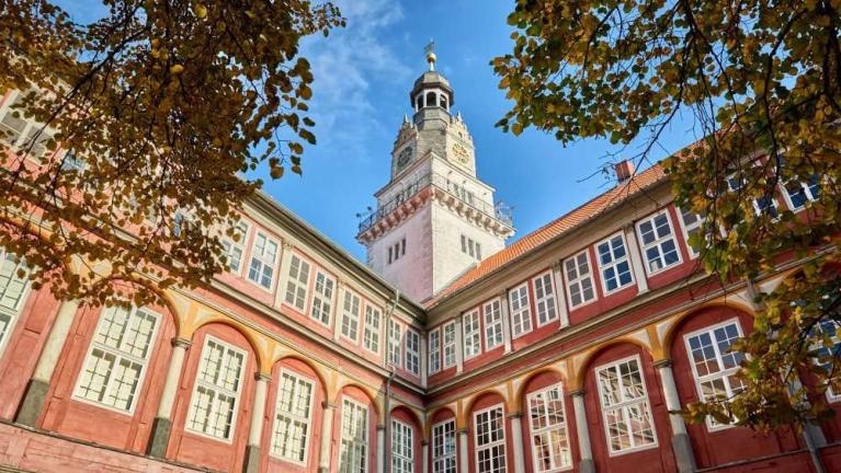 Historisches Gebäude mit Innenhof, roter Fassade, vielen Fenstern und hohem Turm unter blauem Himmel