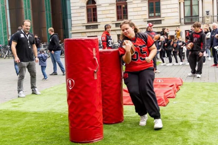 Eine Frau in einem Footballtrikot läuft an roten Trainingspolstern vorbei, während Zuschauer zusehen.