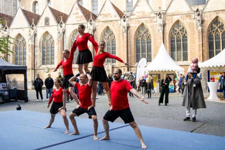Akrobatische Tanzgruppe in roten Oberteilen vor einer historischen Kirche bei einer Veranstaltung im Freien