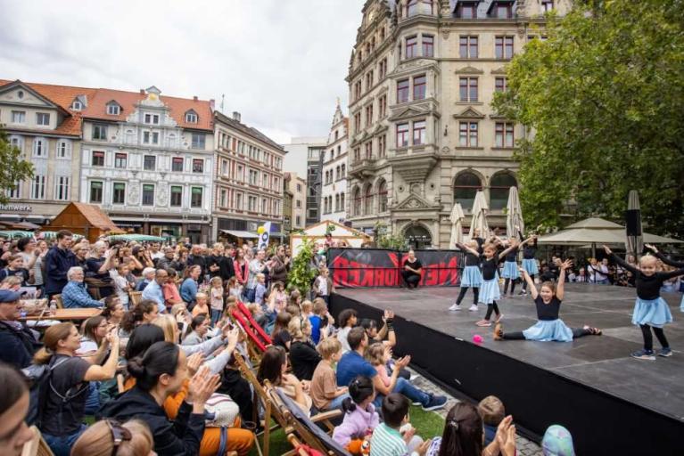 Kinder tanzen auf einer Bühne vor einer großen Menschenmenge auf einem Stadtplatz
