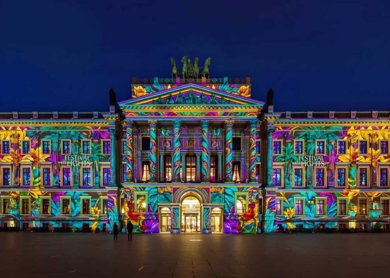 Ein historisches Gebäude wird bei Nacht mit bunten Festival-Lights angestrahlt