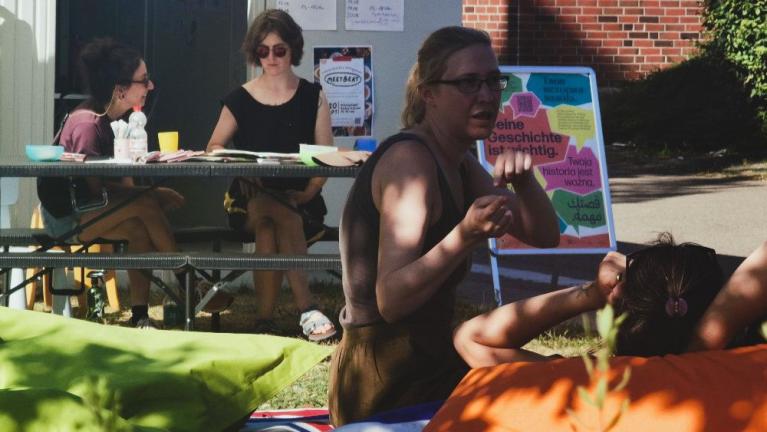 Mehrere Menschen bei einer Outdoor-Veranstaltung mit Tisch und Plakat vor einem Gebäude