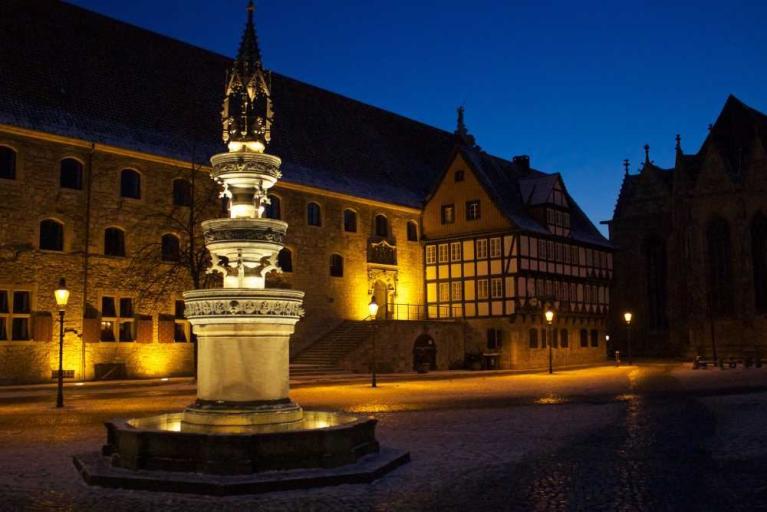 Nachts beleuchteter Platz mit einem Brunnen vor historischen Gebäuden