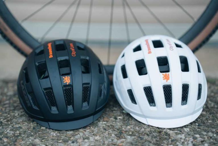 Zwei Fahrradhelme, ein schwarzer und ein weißer, stehen vor einem Fahrradrad