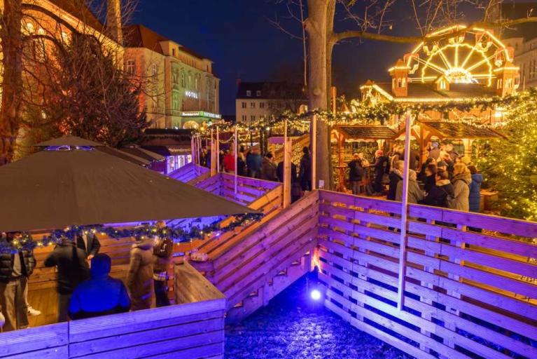 Belebter Weihnachtsmarkt am Abend mit beleuchteten Buden, Menschen und Riesenrad