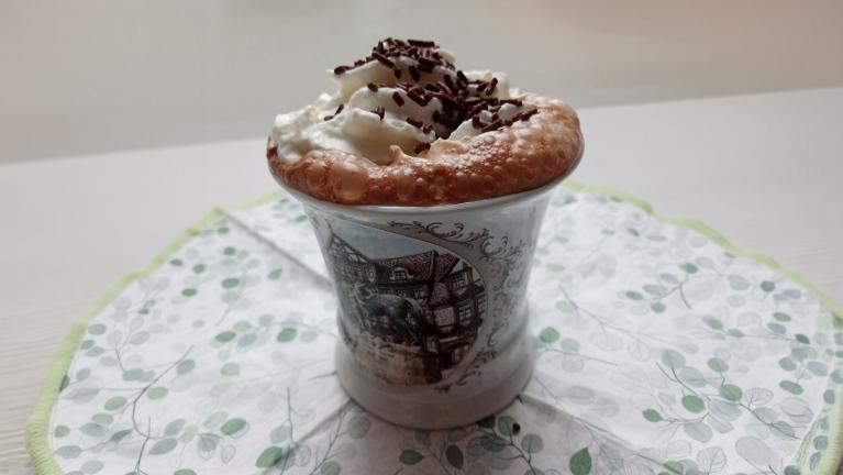 Ein Dessert in einer kleinen Tasse mit Sahne und Schokostreuseln auf einer dekorativen Unterlage