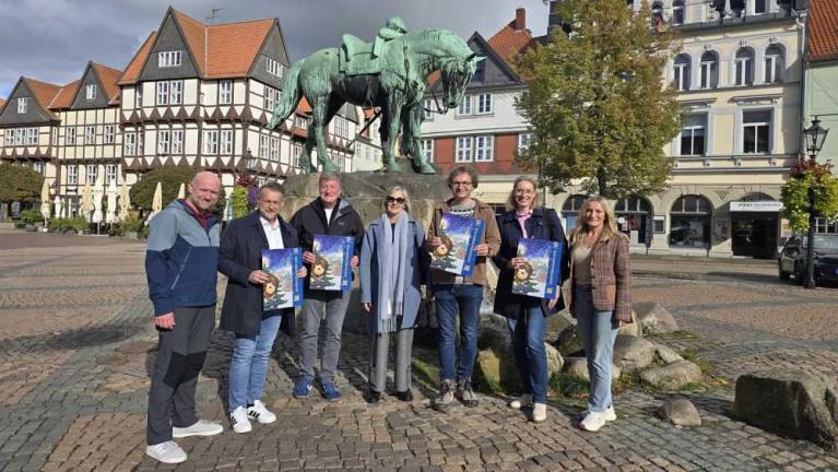 Sieben Personen stehen auf einem Platz vor einer Pferdestatue und halten Plakate in den Händen.