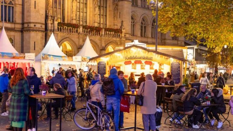Menschen auf einem beleuchteten Herbstmarkt mit Essensständen vor einem historischen Gebäude