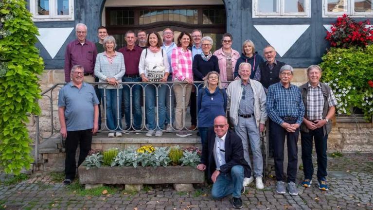 Gruppe von etwa fünfzehn Personen steht und sitzt vor einem historischen Gebäude