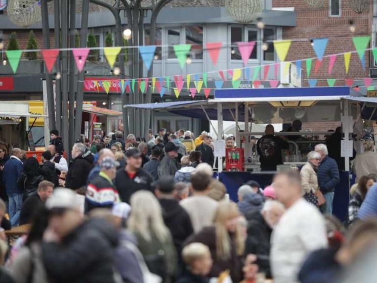 Menschenmenge auf einem belebten Markt mit bunten Wimpelketten und Verkaufsständen