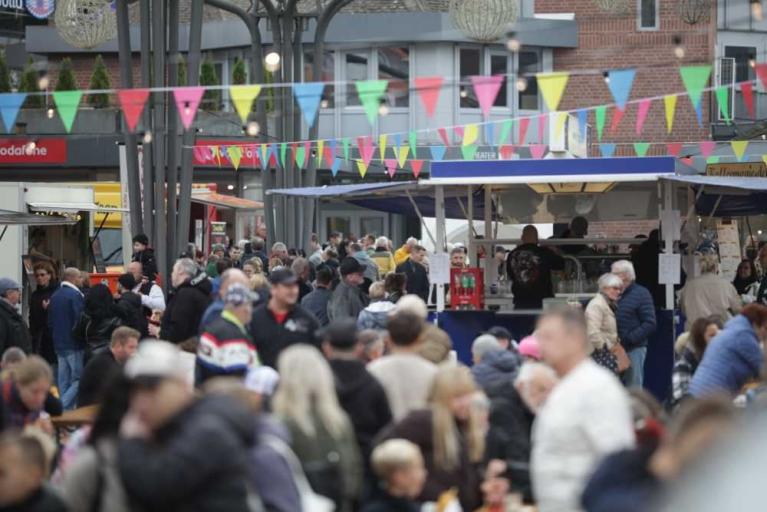 Menschenmenge auf einem belebten Markt mit bunten Wimpelketten und Verkaufsständen