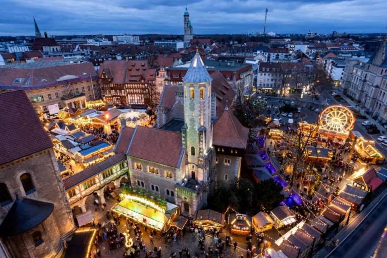 Blick auf einen beleuchteten Weihnachtsmarkt in einer historischen Altstadt mit Kirchturm