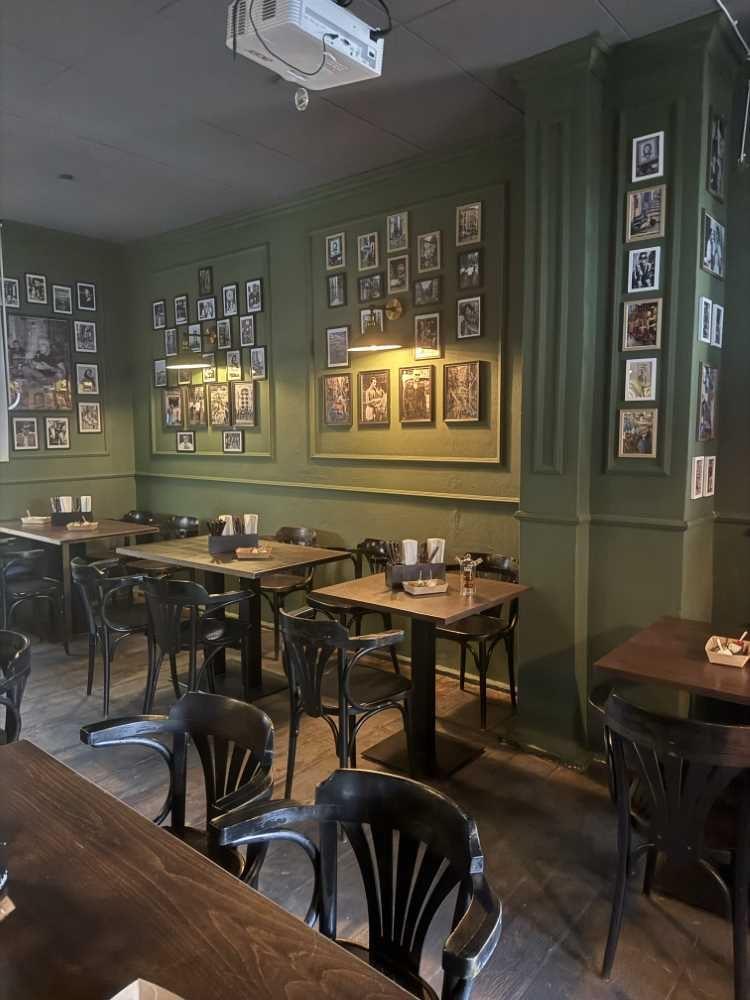 Innenraum eines Cafés oder Restaurants mit grünen Wänden, kleinen Tischen und schwarzen Stühlen