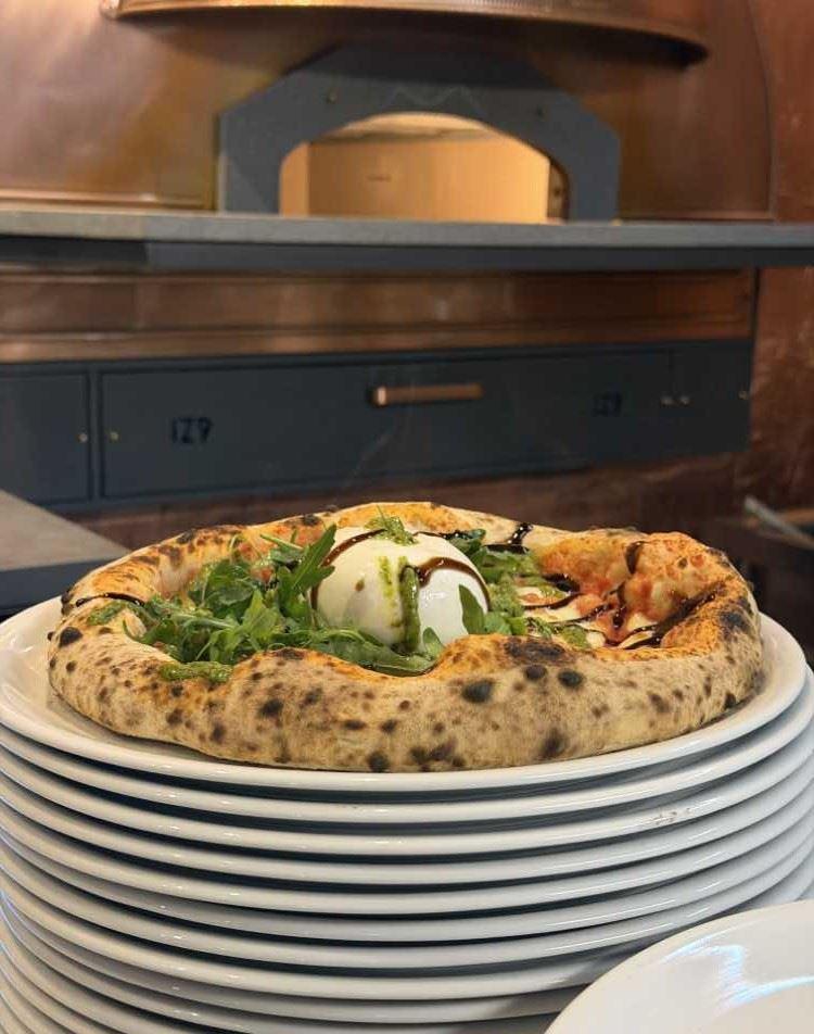 Eine Pizza mit Belag und einer Kugel Burrata auf einem Stapel weißer Teller