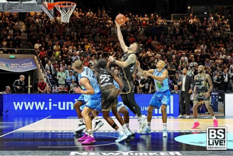 Basketballspiel mit mehreren Spielern unter dem Korb vor vollem Publikum