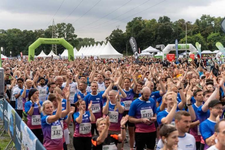 Große Menschenmenge bei einem Lauf- oder Sportevent im Freien, viele Teilnehmer klatschen am Start- oder Zielbereich.
