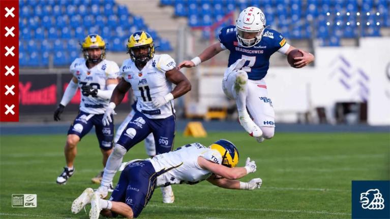 American-Football-Spiel mit einem springenden Spieler in Blau und Verteidigern in Weiß