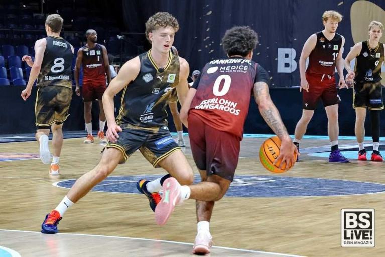 Basketballspiel mit mehreren Spielern auf dem Spielfeld, ein Spieler dribbelt den Ball